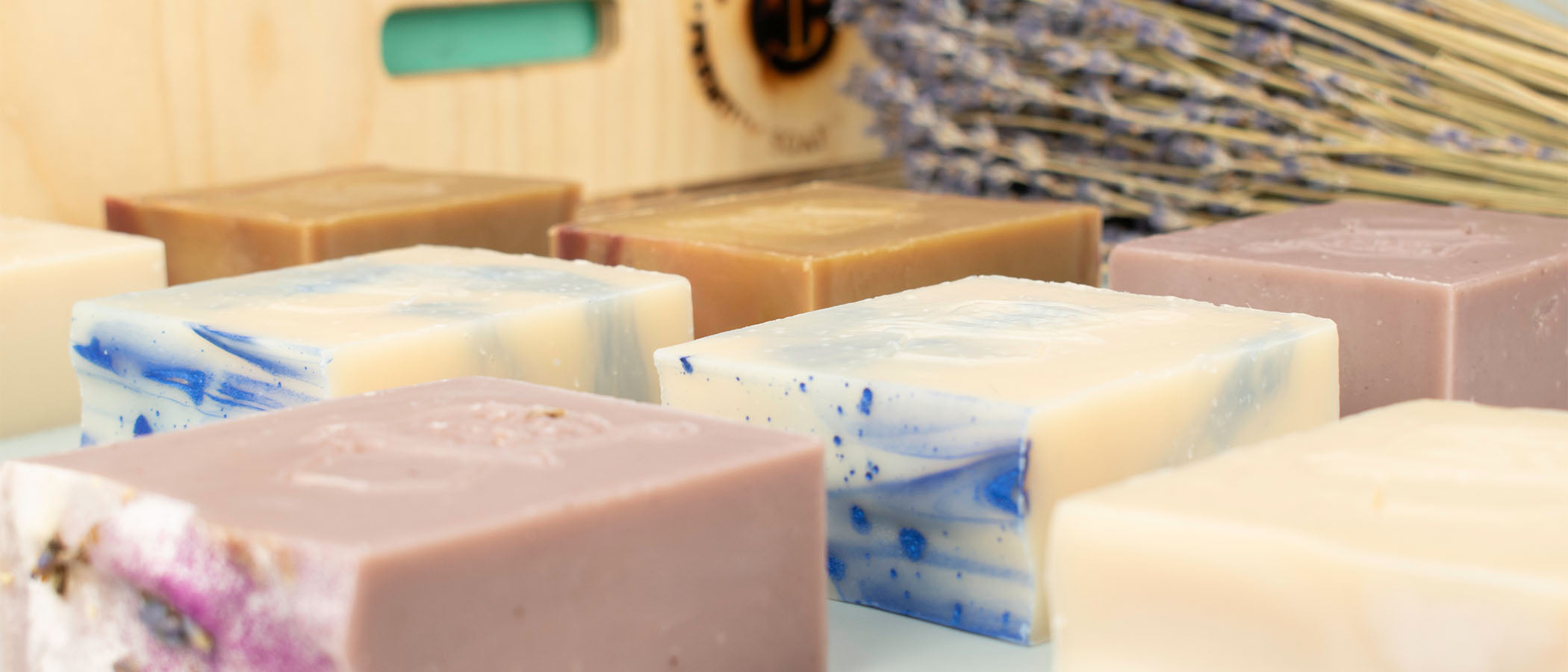 Don Gato Soap Co. homepage hero banner for March featuring the Timeless Favorites restocked collection, showing handcrafted artisan soap bars with lavender and blue swirls, dried botanicals, and a rustic wooden box in bright natural lighting."
