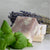 Two bars of white and purple Sleepy Time Natural Soap with dried lavender flower and fresh mint leaves.